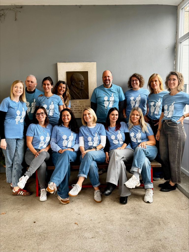Group photo of the 13 project partners in matching light-blue Road2Braille T-shirts, in front of the memorial plaque of Vinko Bek in Zagreb